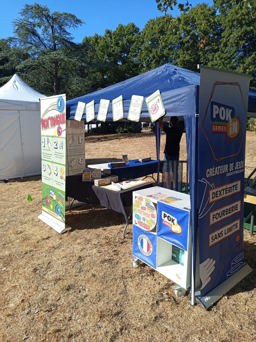 Le stand Pok'in Games sous barnum, avec ses kakémonos et ses tables de jeu en plein air.
